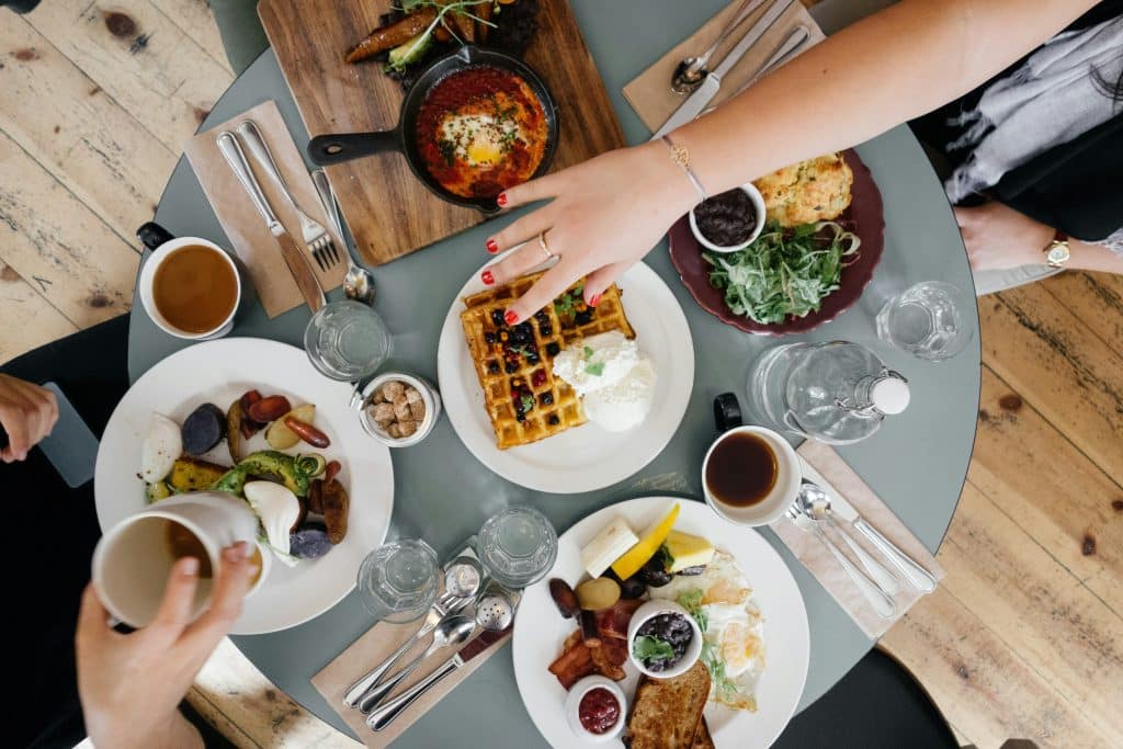 Overhead photo of a group enjoying brunch dishes like waffles and eggs Benedict, representing the social and emotional complexities of eating out with PCOS.