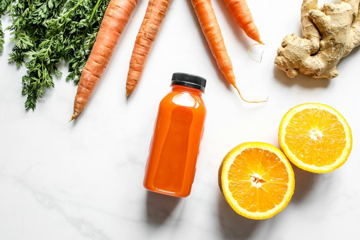 An orange smoothie on a kitchen counter surrounded by fresh ginger, orange slices, and carrots—an example of a more balanced PCOS smoothie rich in fiber and antioxidants to support hormone and blood sugar balance.