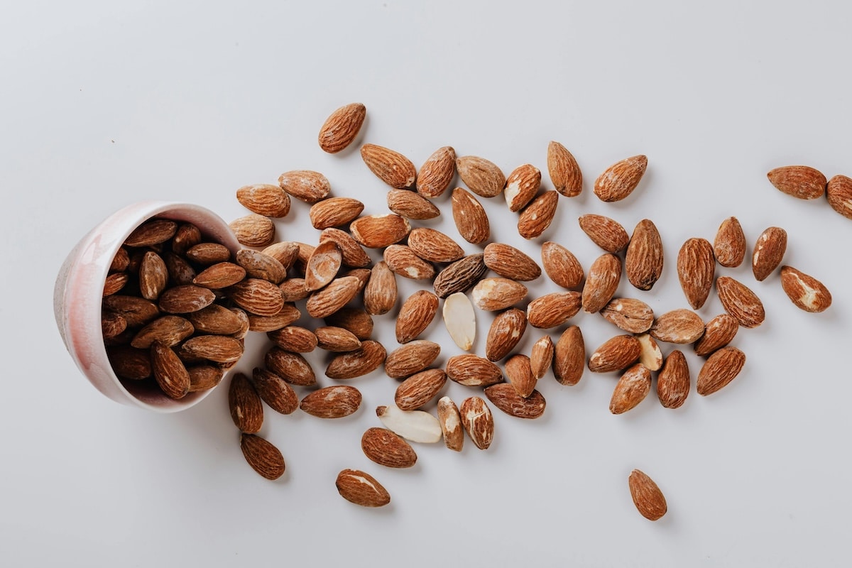 Whole almonds spilling from a ceramic bowl on a white background – a high-protein, PCOS-friendly snack rich in healthy fats.
