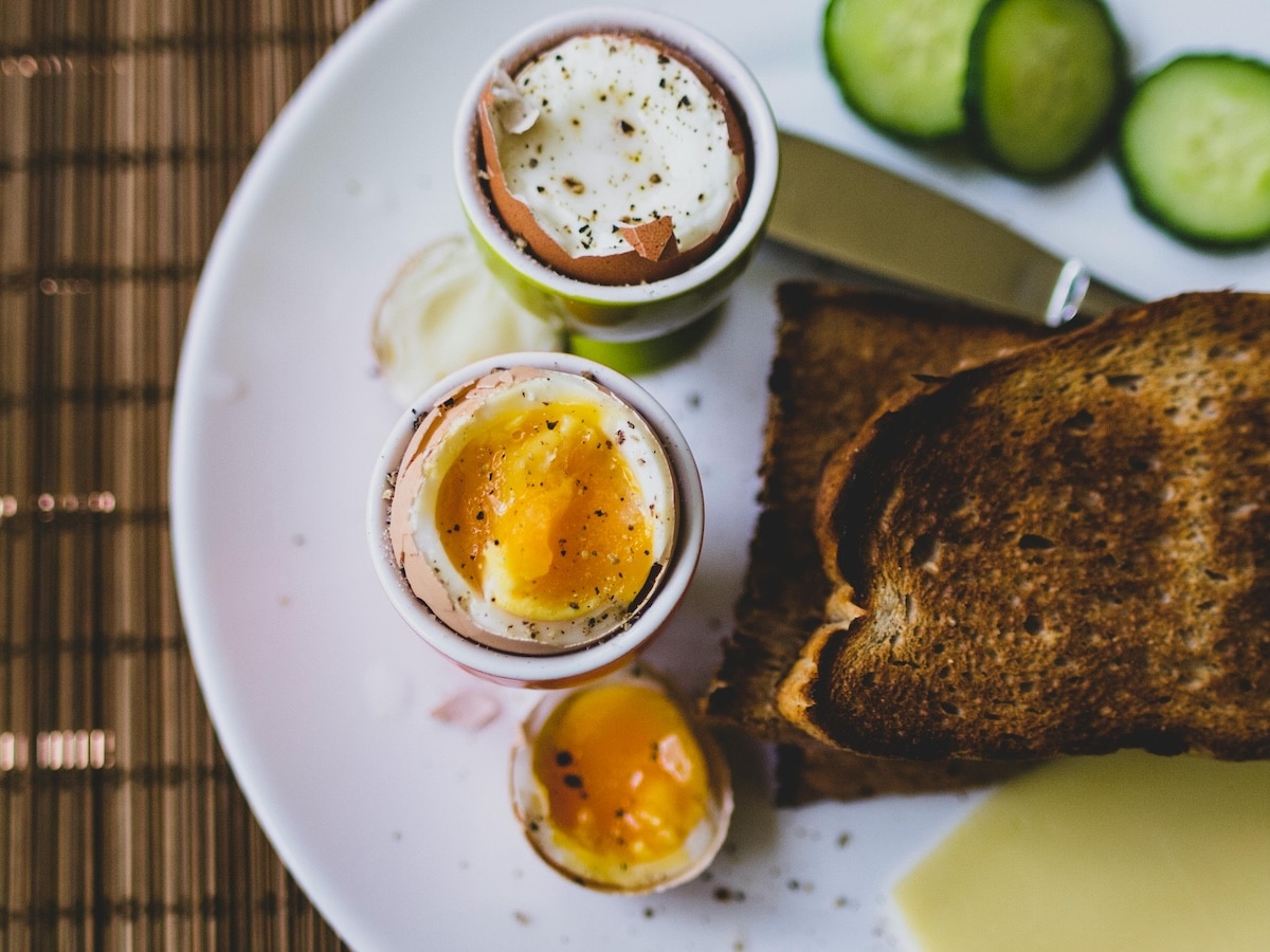 Breakfast with two soft boiled eggs, whole grain toast and cucumber slices. 