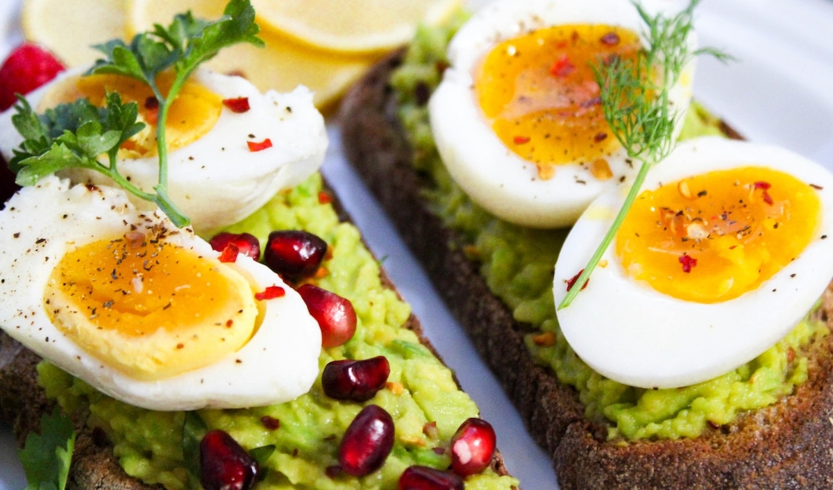 PCOS friendly breakfast idea of rye toast with mashed avocado and hard boiled eggs topped with fresh herbs