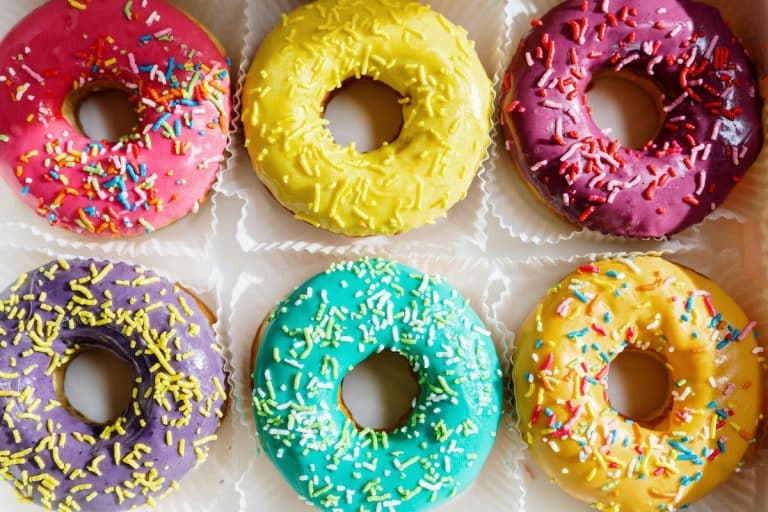 Six donuts dipped in different icing colours topped with spinkles