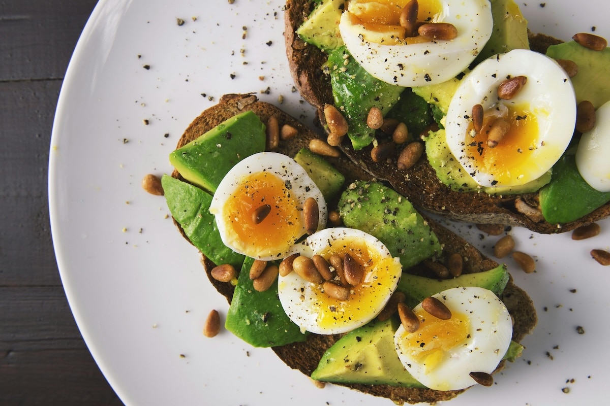 Slices of whole-grain toast topped with avocado and sliced hard-boiled eggs, sprinkled with seasoning for a balanced and nutritious snack.