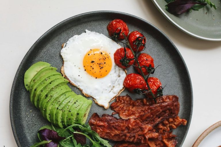 A high-fat, low-carb breakfast with eggs, avocado, bacon, and tomatoes - typical of keto meal patterns explored for PCOS.