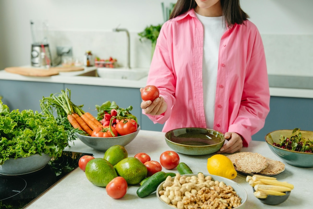 Woman considering a tomato surrounded by fresh vegetables—exploring high-fiber food choices for a PCOS-friendly diet.