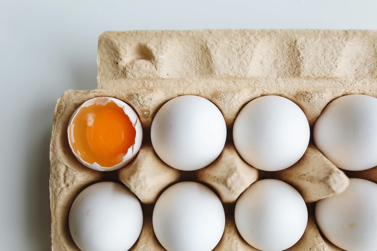 Eggs in a carton, with one cracked to show the yolk—rich in protein and choline, essential fertility foods for PCOS and reproductive health.