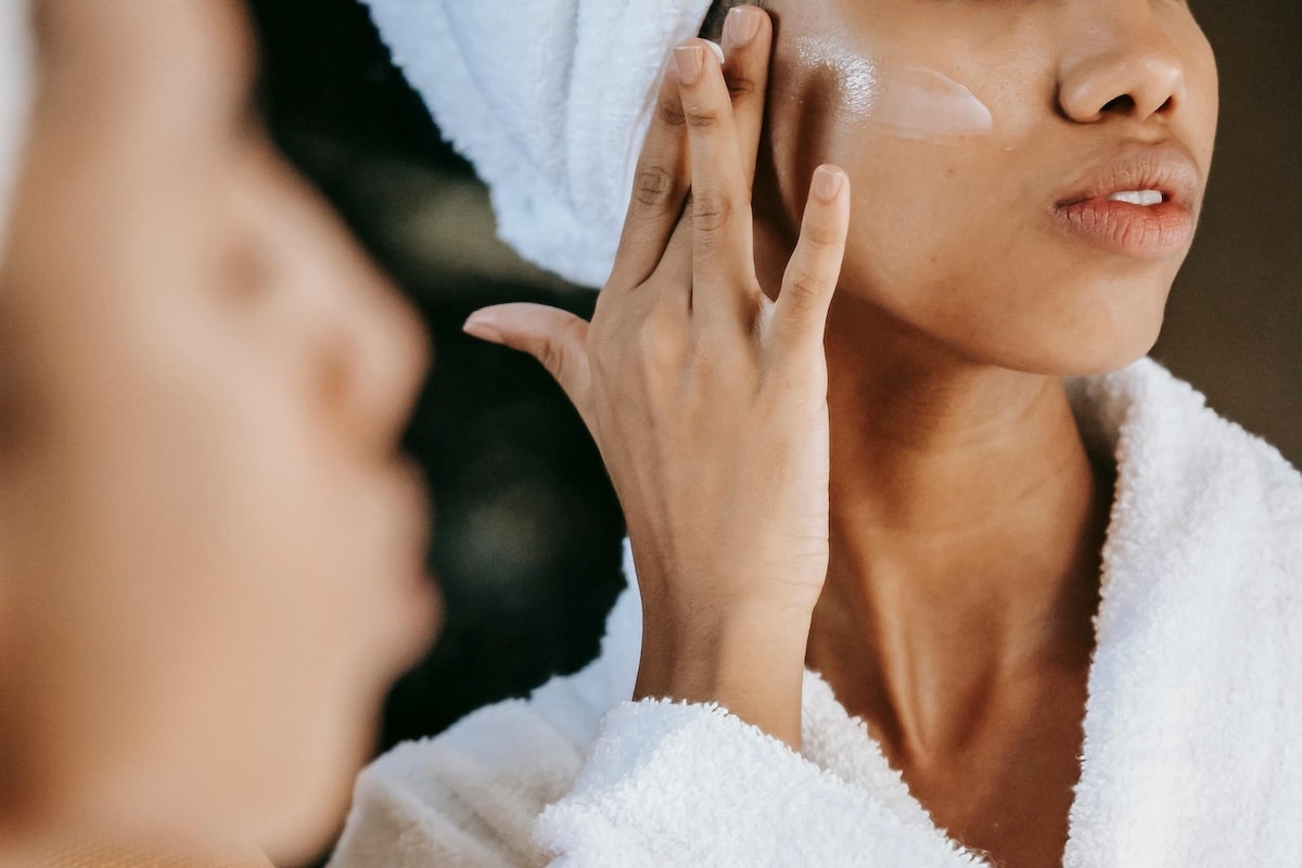 Woman gently applying face cream while looking in the mirror, reflecting a calm, natural approach to skincare and hormonal acne.
