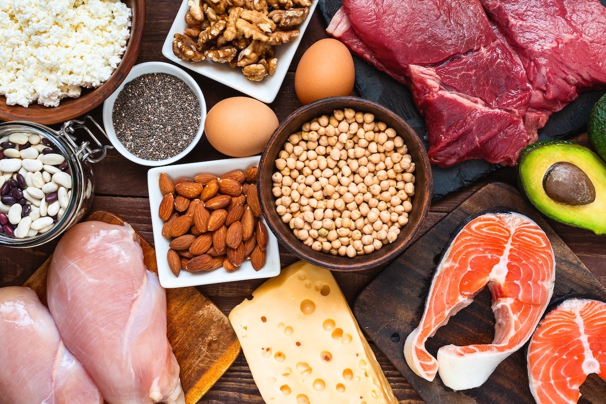 Aerial view of high-protein and healthy fat foods including chicken breast, eggs, salmon, red meat, beans, almonds, chia seeds, cheese, and avocado, illustrating dietary strategies to stay full and manage appetite for women with PCOS after stopping Ozempic.